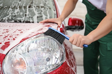 Photo of Male worker cleaning vehicle with brush at car wash