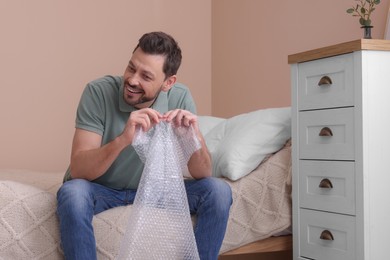 Photo of Man popping bubble wrap in bedroom at home. Stress relief