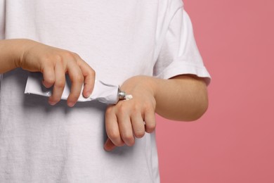 Photo of Child applying ointment onto hand against pink background, closeup. Space for text