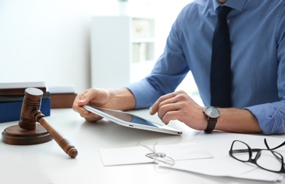 Photo of Notary working with tablet and judge gavel on table, closeup. Law and justice concept