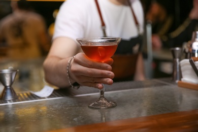 Photo of Bartender with glass of tasty cocktail at counter in nightclub, closeup