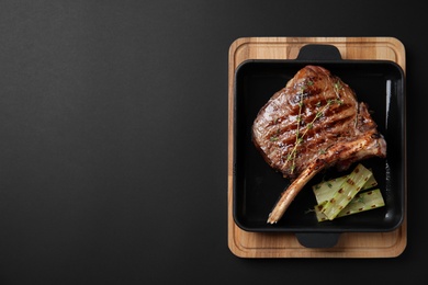 Photo of Grill pan with meat on black background, top view. Space for text