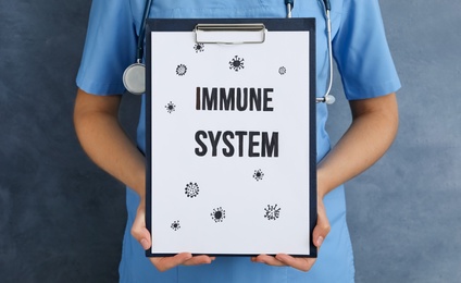 Photo of Woman holding clipboard with phrase Immune System on blue background, closeup