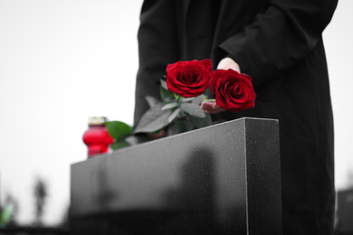 Photo of Woman with red roses near black granite tombstone outdoors, closeup. Funeral ceremony