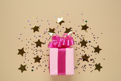 Photo of Pink gift box and shiny confetti on beige background, top view
