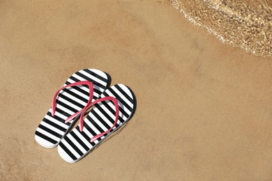 Photo of Stylish flip flops on sandy beach near sea, above view. Space for text