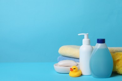 Photo of Baby cosmetic products, bath duck, sponge and towels on light blue background. Space for text