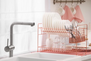 Photo of Sink and drying rack with clean dishes and cutlery on countertop in kitchen