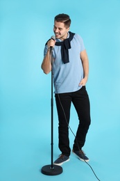 Young handsome man in casual clothes singing with microphone on color background