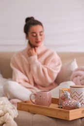 Photo of Beautiful young woman relaxing at home, focus on tray with cup of drink. Cozy atmosphere