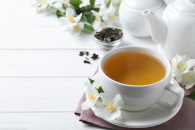 Photo of Cup of tea and fresh jasmine flowers on white wooden table. Space for text