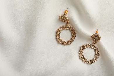 Photo of Elegant golden earrings on white fabric, flat lay with space for text. Stylish bijouterie
