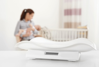 Photo of Modern baby scales on table and blurred woman with child indoors. Space for text
