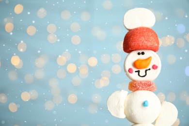Photo of Funny snowman made of marshmallows against blurred festive lights, closeup. Space for text