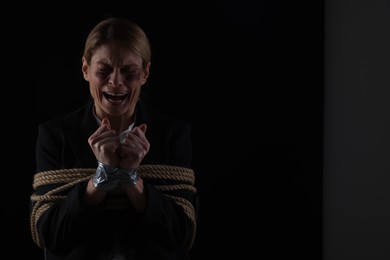 Photo of Scared woman tied up and taken hostage on dark background. Space for text