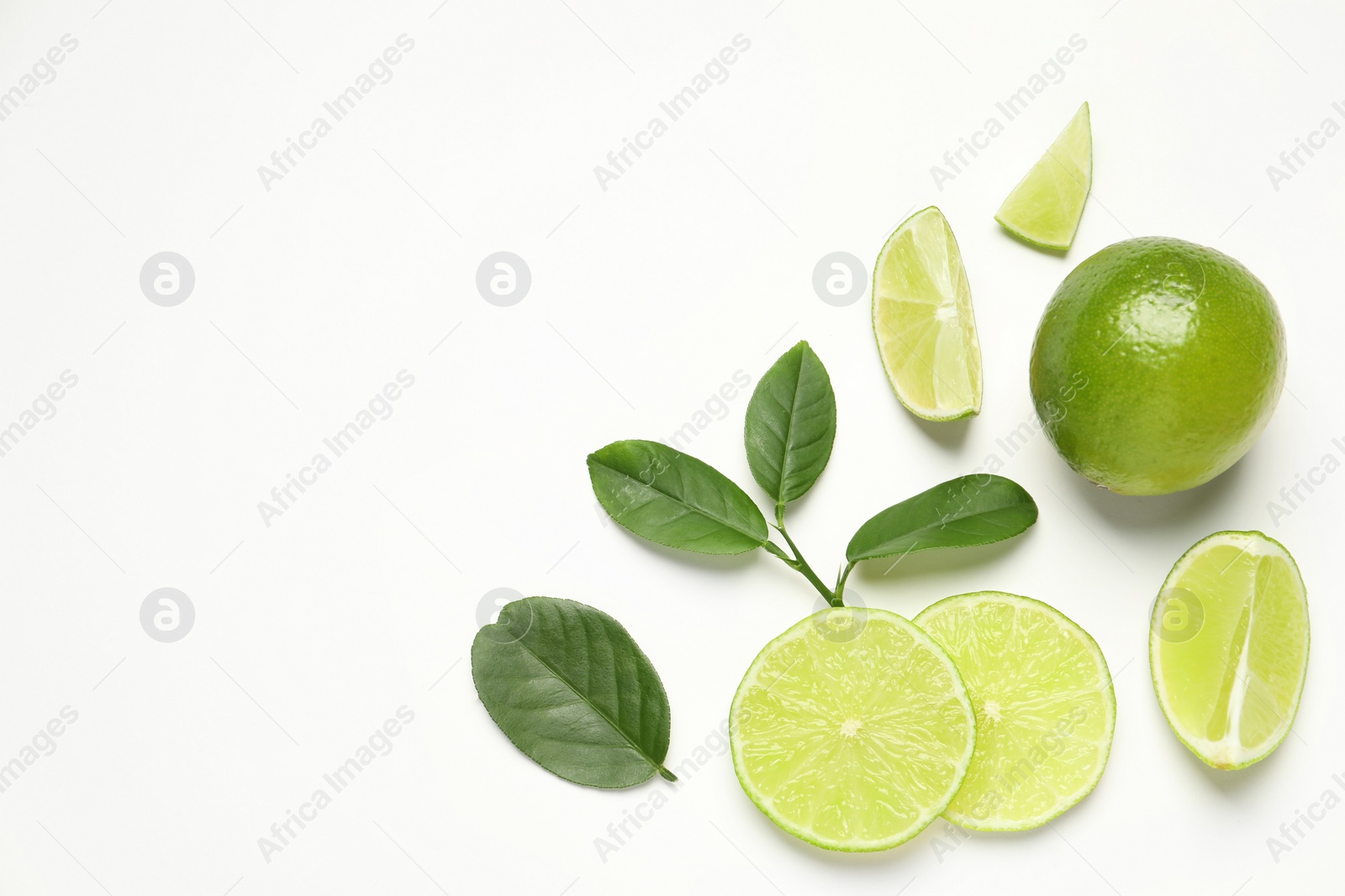 Photo of Whole and cut fresh ripe limes with green leaves on white background, flat lay