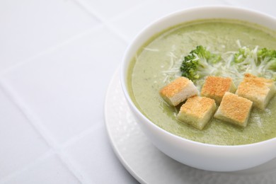 Photo of Delicious broccoli cream soup with croutons and cheese on white tiled table, closeup. Space for text