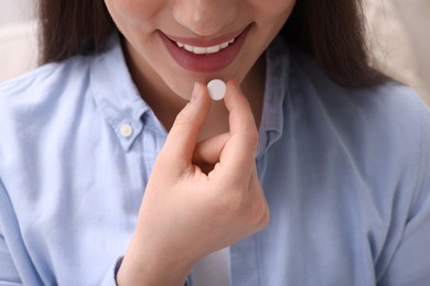 Woman taking pill on blurred background, closeup view