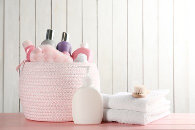 Photo of Basket with different baby cosmetic products and bathing accessories on pink wooden table