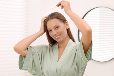 Photo of Beautiful woman applying serum onto hair indoors