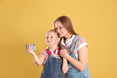 Photo of Happy mother and little daughter taking selfie on yellow background