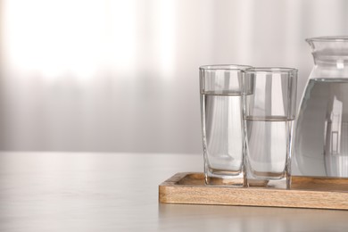Photo of Glasses and jug with water on white table against blurred background. Space for text