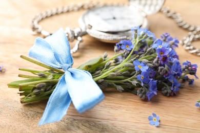 Photo of Beautiful blue forget-me-not flowers tied with ribbon on wooden table, closeup