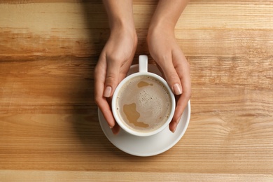 Photo of Woman holding cup of coffee at wooden table, top view