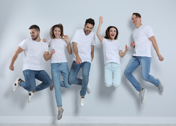 Photo of Group of young people in stylish jeans jumping near light wall