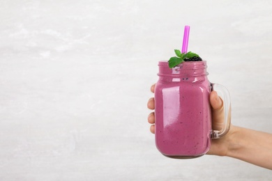 Photo of Young woman holding mason jar of tasty blackberry smoothie on light grey background, closeup. Space for text