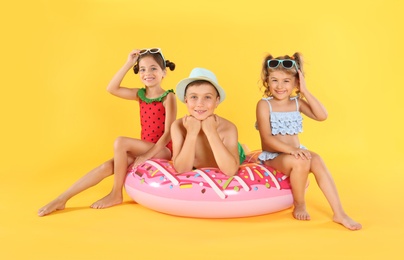 Photo of Cute little children in beachwear with bright inflatable ring on yellow background