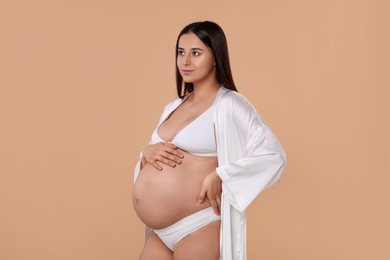 Photo of Beautiful pregnant woman in stylish comfortable underwear and robe on beige background