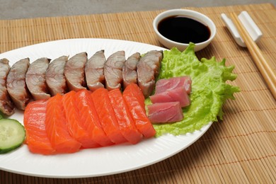 Photo of Delicious mackerel, salmon and tuna served with lettuce and soy sauce on table, closeup. Tasty sashimi dish