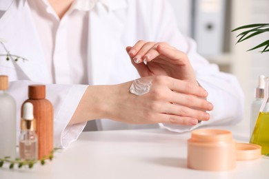 Photo of Dermatologist applying cream onto hand at white table indoors, selective focus. Testing cosmetic product