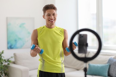 Photo of Smiling sports blogger working out with dumbbells while streaming online fitness lesson at home