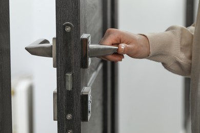 Photo of Woman opening wooden door indoors, closeup of hand on handle