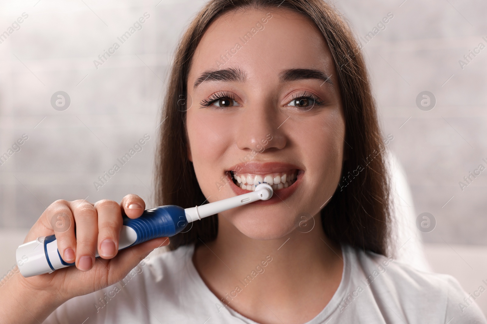 Photo of Young woman brushing her teeth with electric toothbrush in bathroom, closeup