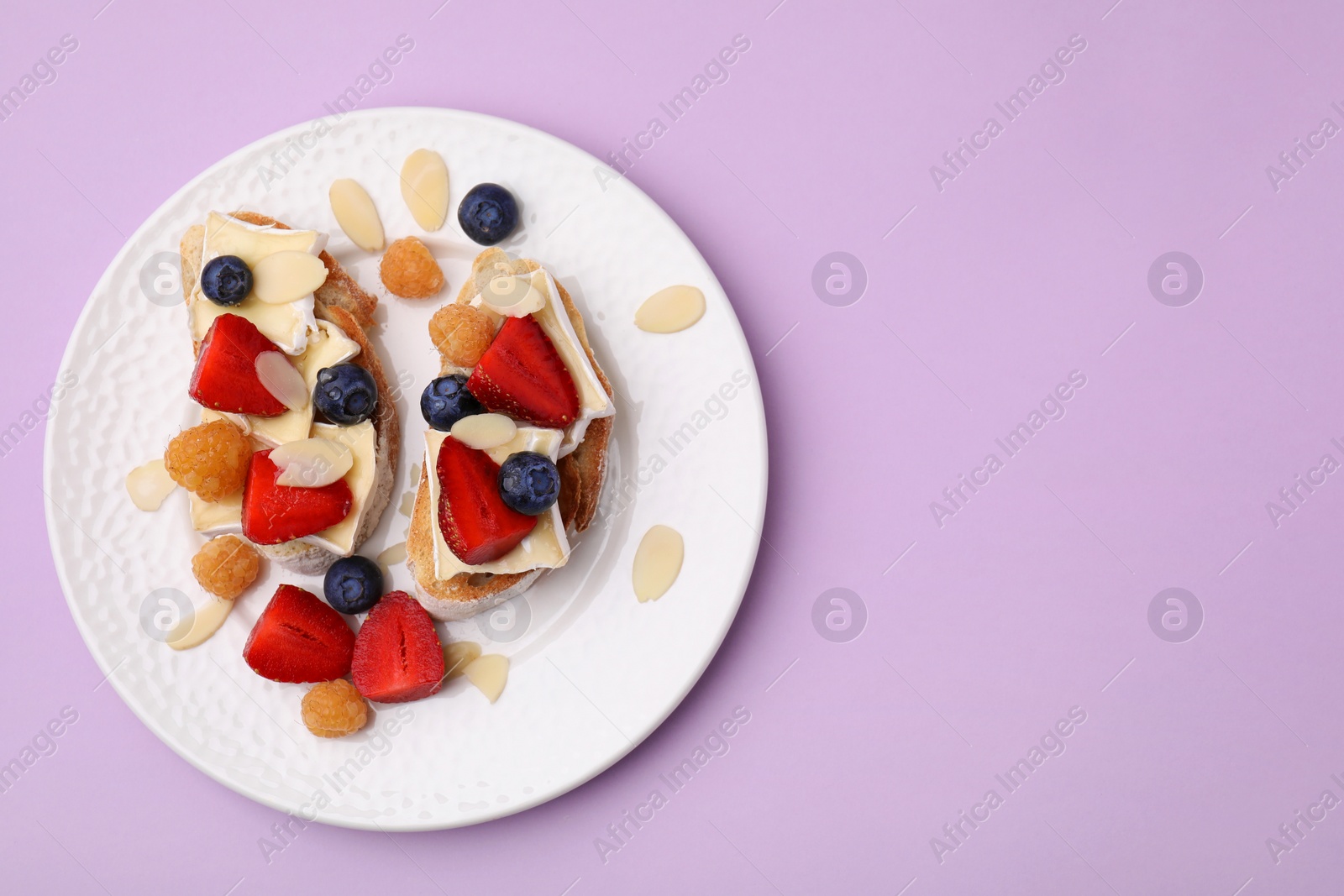 Photo of Tasty sandwiches with brie cheese, fresh berries and almond flakes on violet background, top view. Space for text