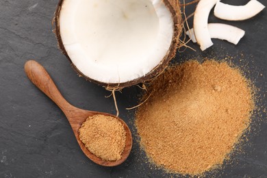 Photo of Coconut sugar, spoon and fruit on dark textured table, flat lay