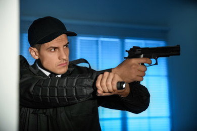 Photo of Professional security guard with flashlight and gun in dark room