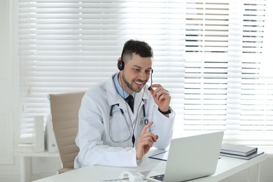 Photo of Doctor with headset consulting patient online at desk in clinic. Health service hotline