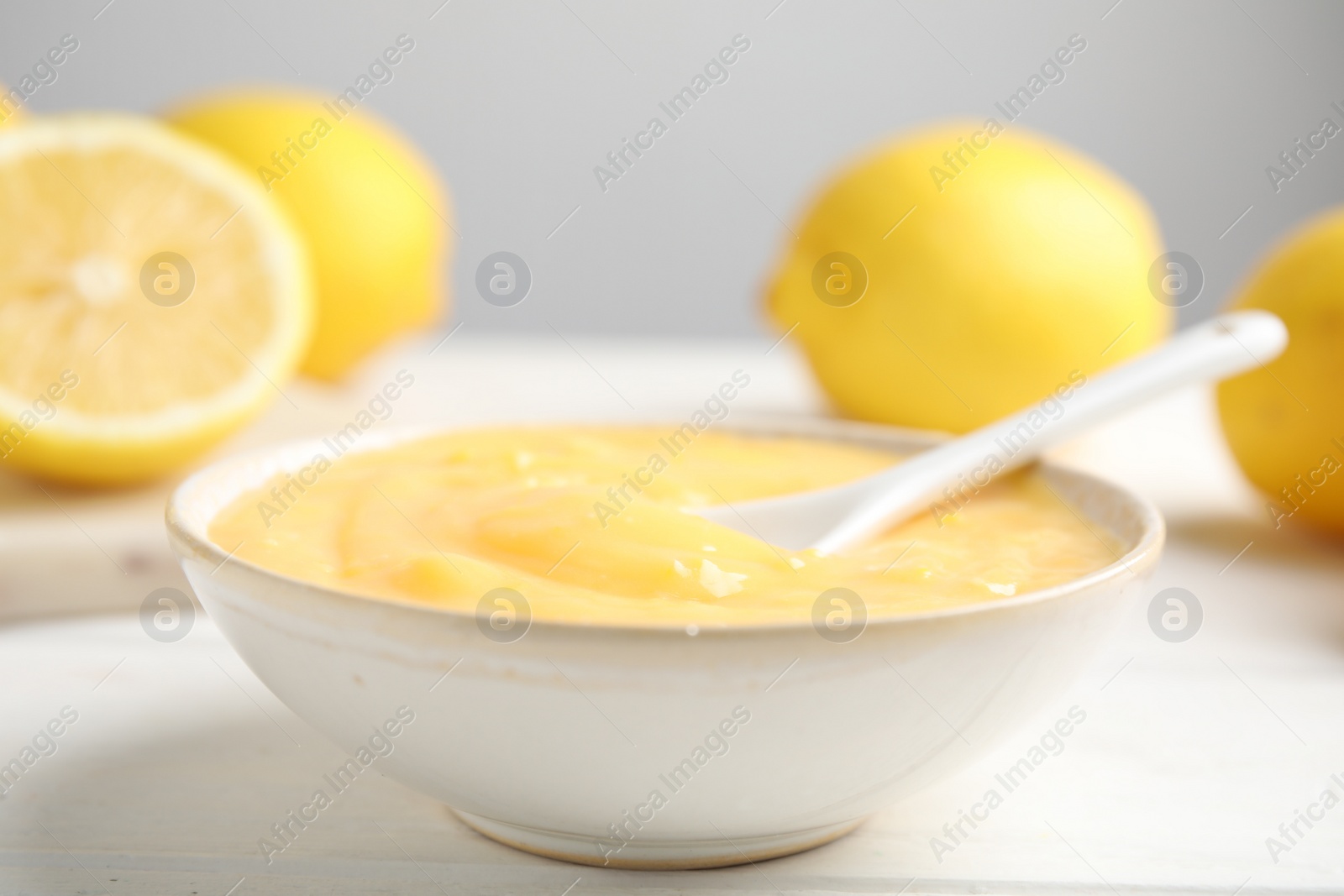 Photo of Delicious lemon curd in bowl on white wooden table, closeup