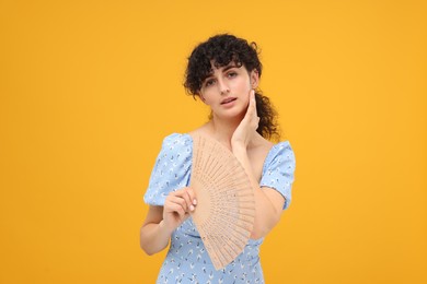 Photo of Woman with hand fan suffering from heat on orange background