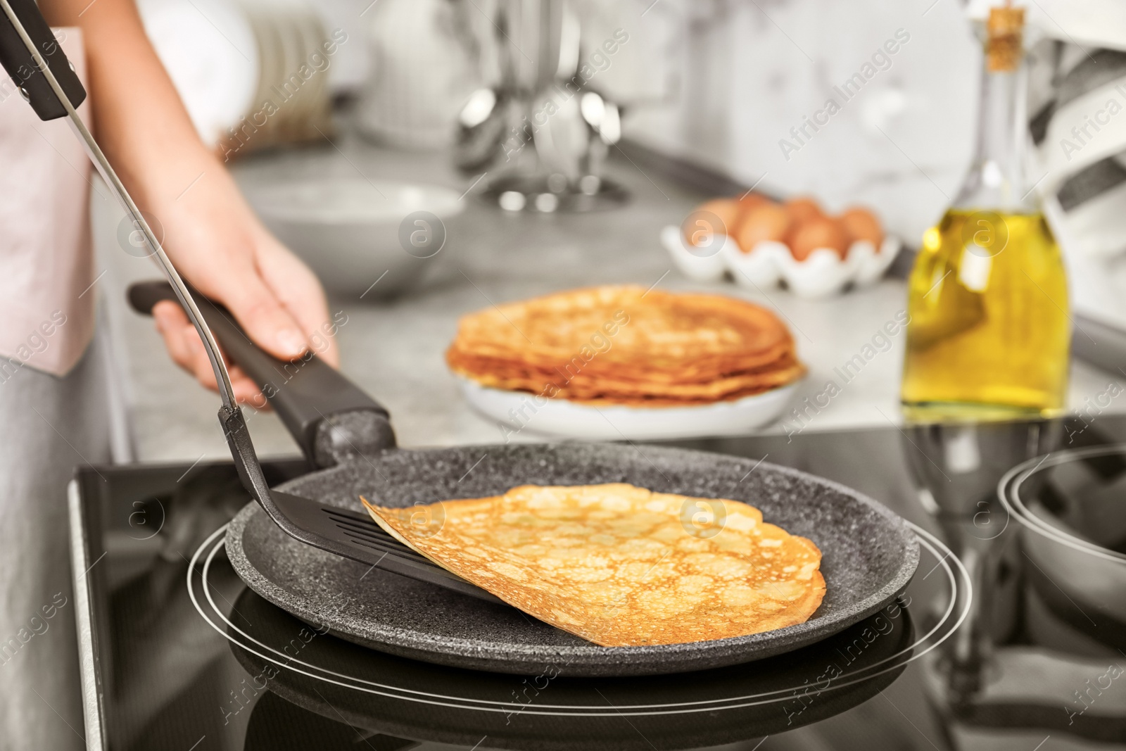 Woman cooking delicious thin pancakes on induction stove, closeup Photo of Woman cooking delicious thin pancakes on induction stove, closeup