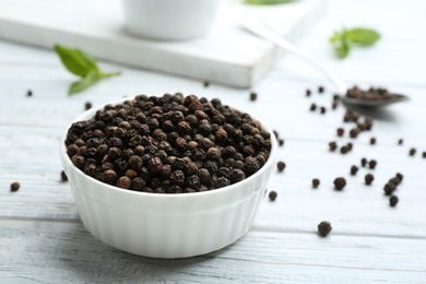 Photo of Bowl of black pepper corns on white wooden table, space for text