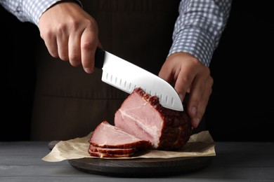 Photo of Man cutting ham on wooden board at table, closeup