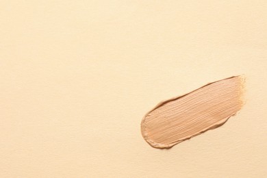 Photo of Smear of skin foundation on beige background, top view. Space for text