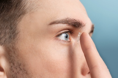 Photo of Young man putting contact lens in his eye on color background