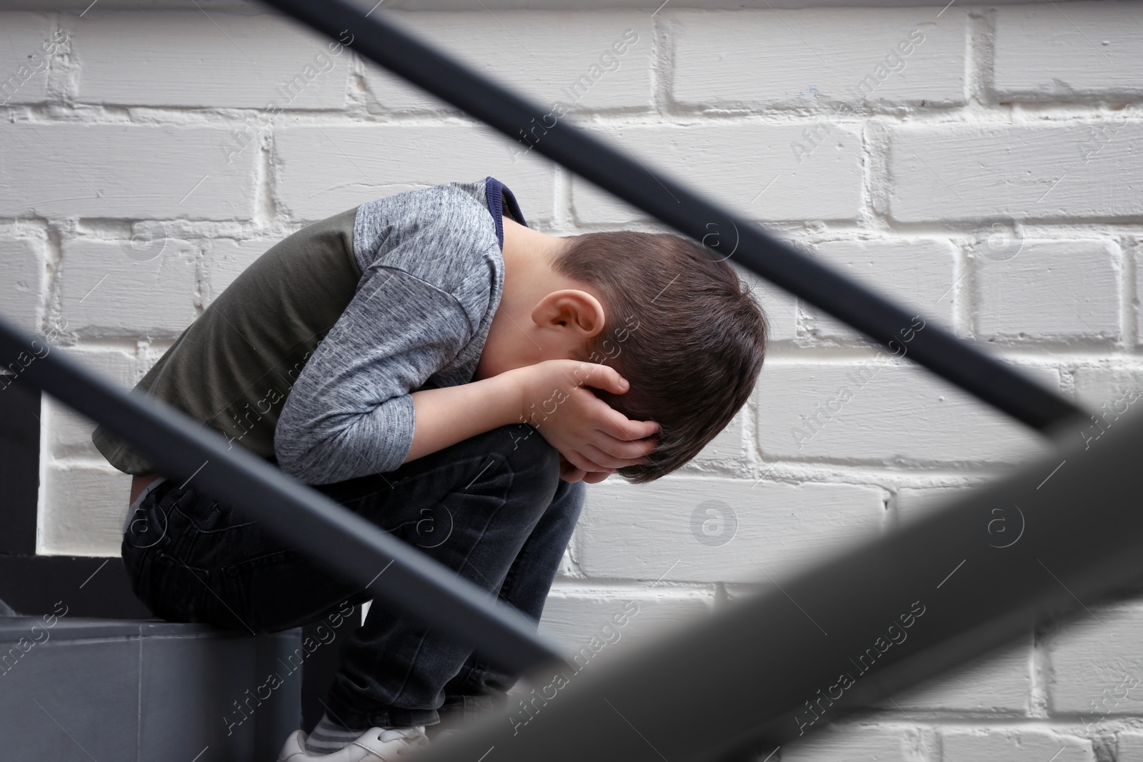 Photo of Sad little boy sitting on stairs indoors