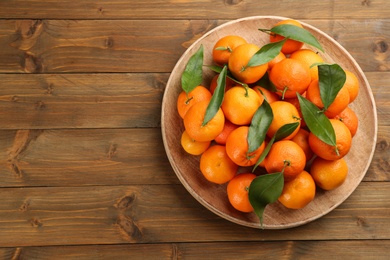 Photo of Fresh ripe tangerines with green leaves on wooden table, top view. Space for text
